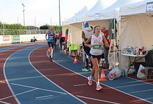 Competitive female runner smiling at a track event in Great Britain, close to the finish line, during a marathon or race with support tents in the background, highlighting endurance and athletic achievement.