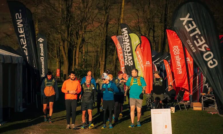 Energetic trail runners gathering at a night race event, showcasing running gear and hydration as they prepare for a marathon in the woods.