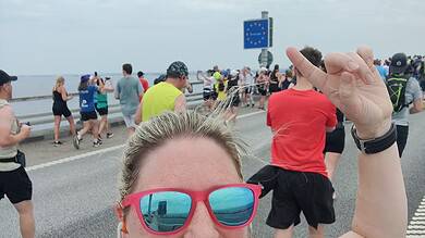 Bright smiling female runner taking a selfie during a marathon or outdoor running event on a scenic coastal route with a large crowd of participants, reflecting running insights and marathon training outdoors.
