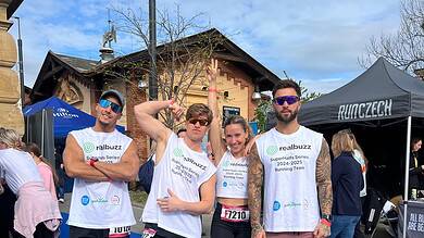 1. Group of runners at a marathon event wearing running team shirts, smiling and posing on a blue running mat after completing a race, with race bibs visible.