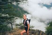 An adventurous woman trail running through lush forest terrain, showcasing ASICS trail shoes designed for outdoor running and exploration.