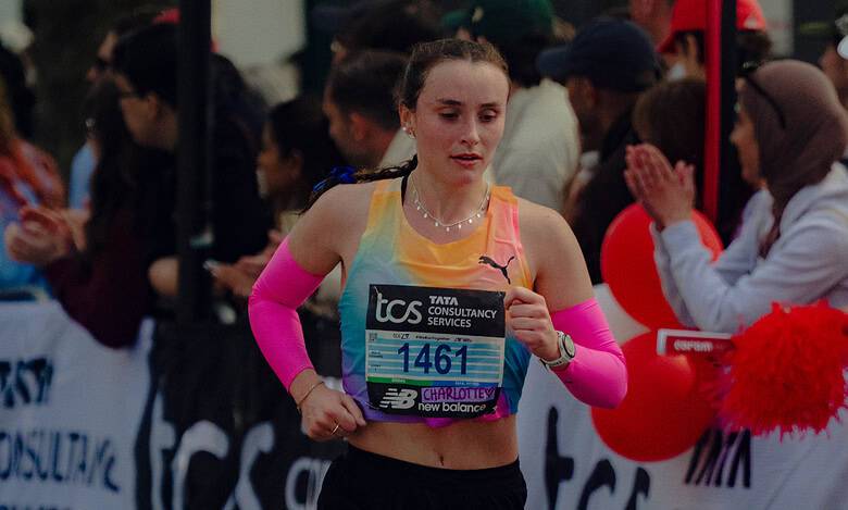 Female marathon runner in race, wearing pink arm sleeves and running shoes, with bib number 1461, competing in a city marathon event.