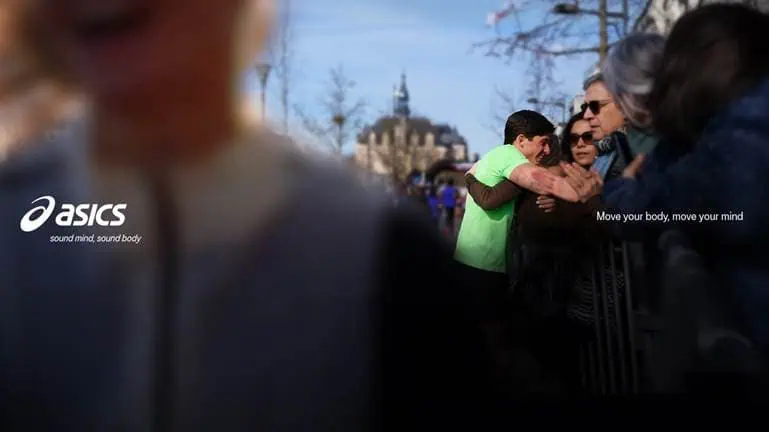Group of runners and spectators at a running event, with ASICS branding and a motivational slogan, capturing the energy and community spirit of running.