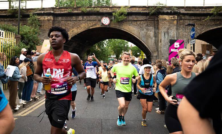 Runners participating in the Hackney Half Marathon, supporting the Single Homeless Project charity, with spectators and a historic bridge in the background.
