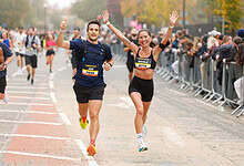 Two runners celebrating crossing the finish line at the Manchester Half Marathon, with cheering spectators and autumn trees in the background.