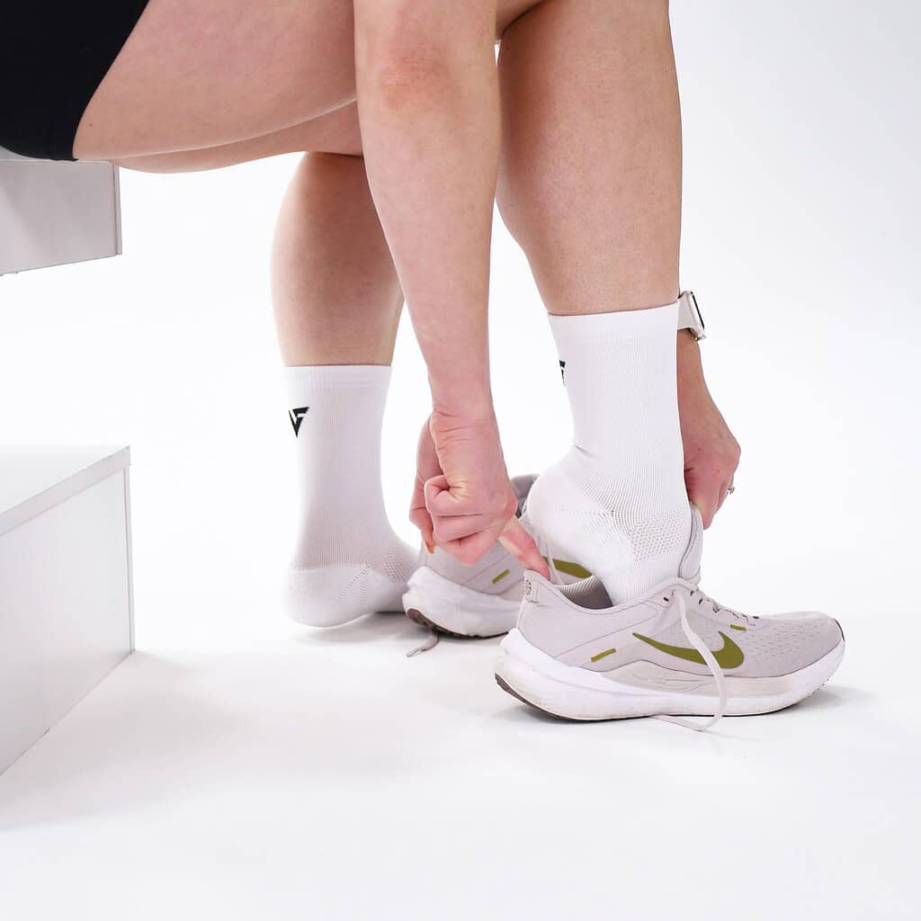 Close-up of a person tying running shoes while wearing Velocity Performance Crew Socks Adult (2 Pairs) for optimal athletic comfort.