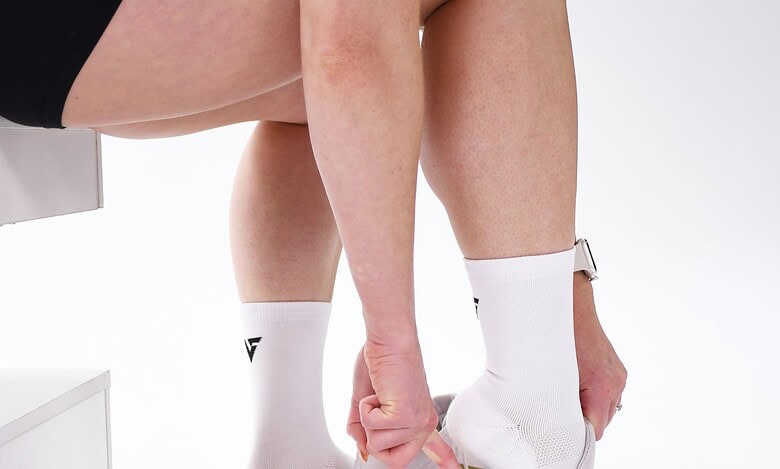 Close-up of a person tying running shoes while wearing Velocity Performance Crew Socks Adult (2 Pairs) for optimal athletic comfort.