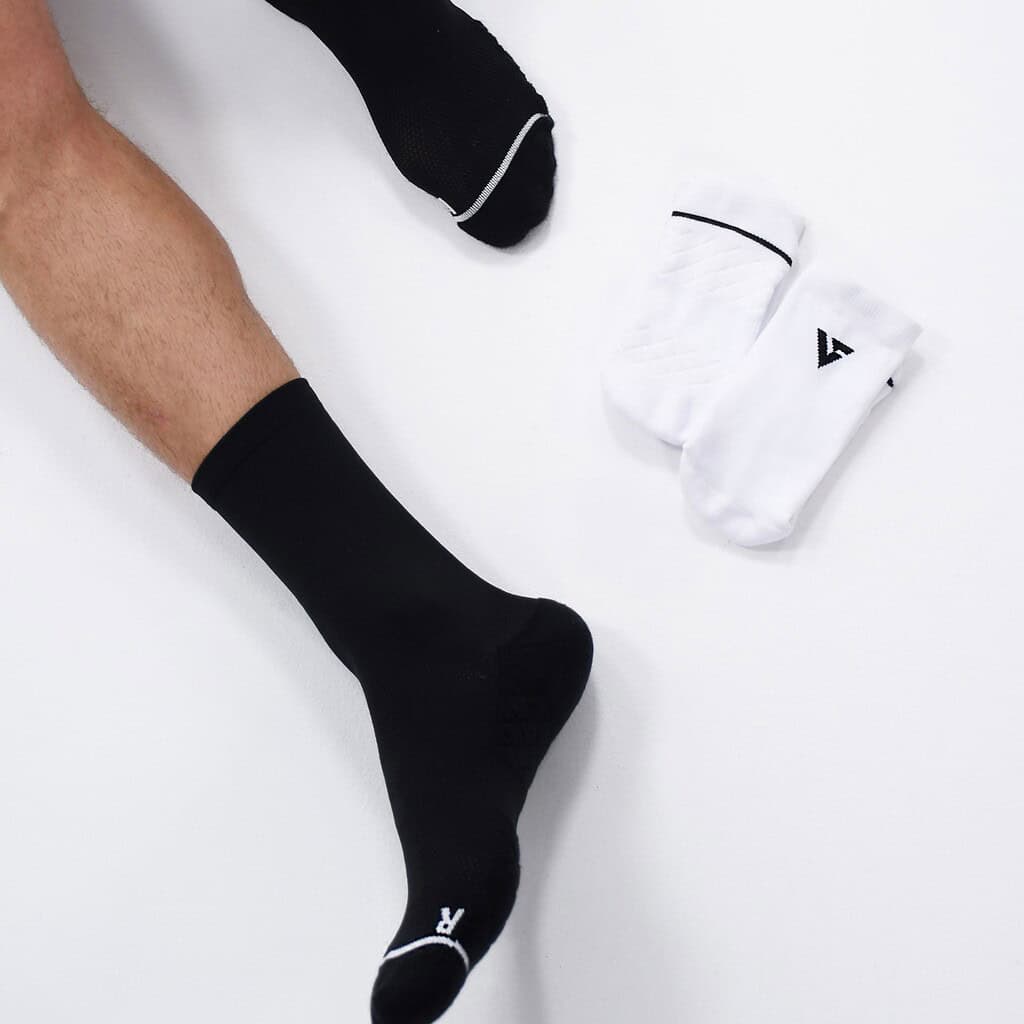 Close-up of a person's leg wearing a black running sock, with a pair of white running socks nearby on a white background.