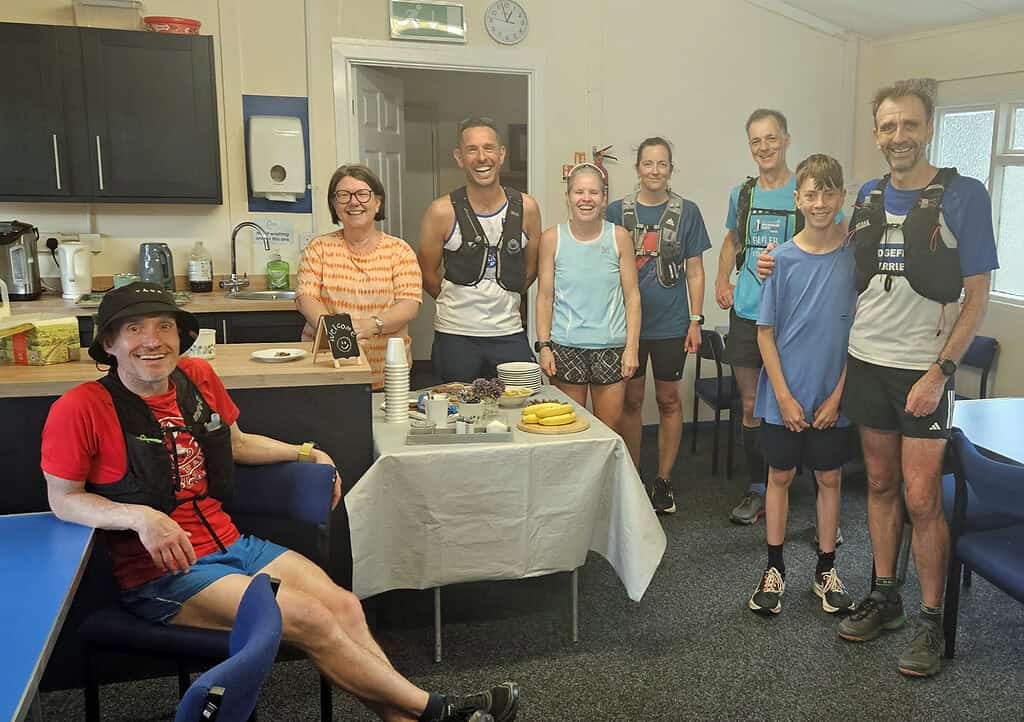Running group celebrating after a training session in a community centre, wearing running gear and hydration vests, with a cheerful atmosphere and diverse participants.