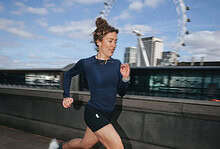 Female runner in athletic gear running along a riverbank with the London Eye in the background on a clear day.