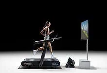 Woman running on a treadmill with virtual outdoor scenery on screen, showcasing indoor running and virtual training technology.