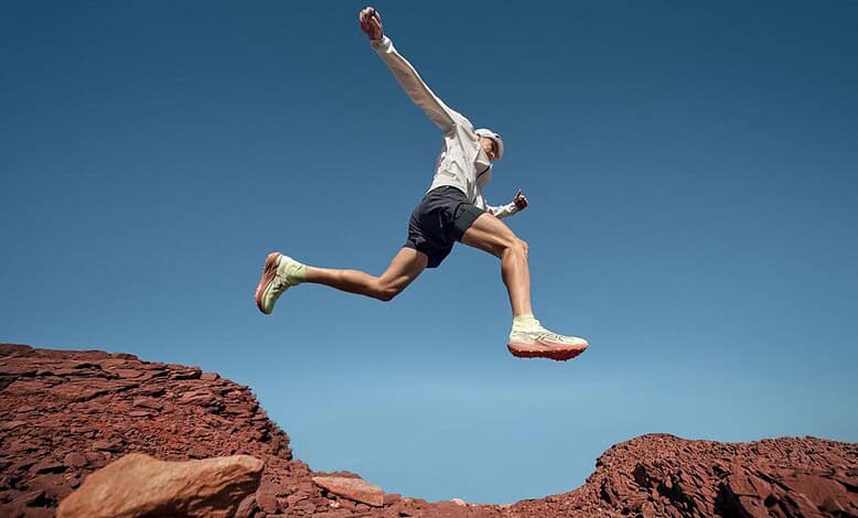 A trail runner in mid-air jump over rocky terrain during outdoor run, showcasing agility and endurance in nature.