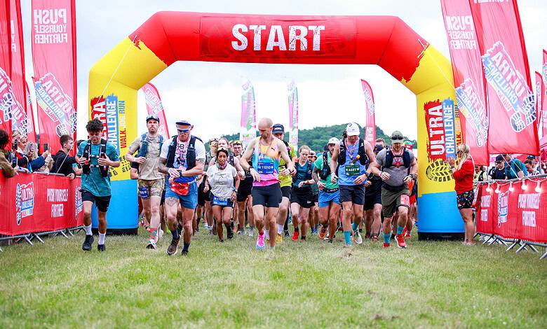Runners start the Peak District Ultra Challenge at the starting line under a red and yellow inflatable arch.