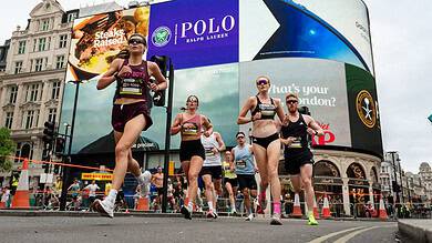 Group of runners participating in the London 10K race, with iconic Trafalgar Square buildings and digital advertising billboards in the background.