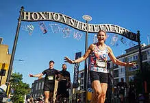 Female runner celebrating crossing the finish line at Hoxton Street Market during Saucony Run Shoreditch Half 2026 event.