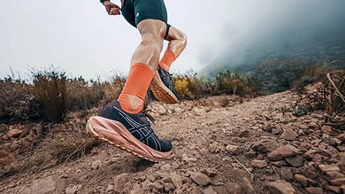 Runner in trail shoes and orange socks running on a rugged mountain trail with misty background.