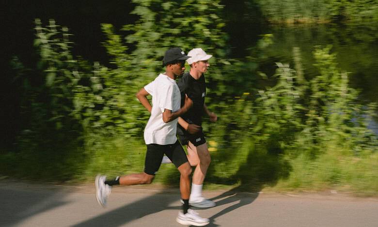 Two runners, a man and a woman, jogging along a scenic riverside path surrounded by lush greenery.
