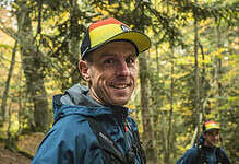 Male trail runner in colourful cap and waterproof jacket smiling in a forest during autumn.