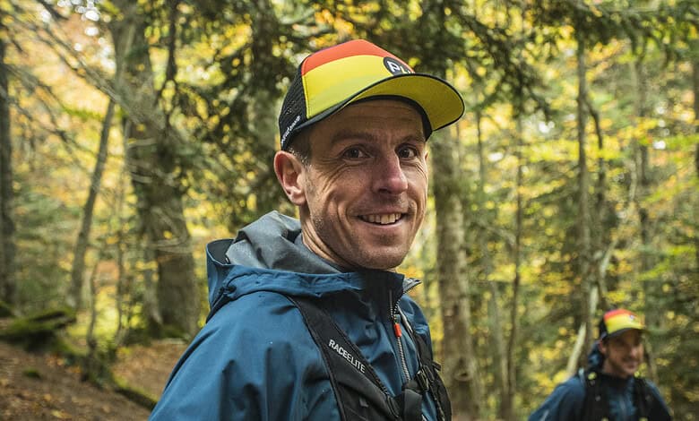 Male trail runner in colourful cap and waterproof jacket smiling in a forest during autumn.