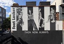 Black and white mural of four people sitting and standing, with 'Foot Locker' text and 'Then. Now. Always.' slogan on a city wall.