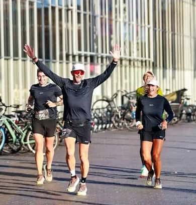Group of runners celebrating with arms raised after completing a race in an urban setting with bicycles in the background.