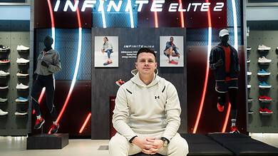 Jonathan Hutnyan sitting in front of Under Armour Infinite Elite 2 running shoes display at a store.