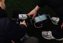 Two runners reviewing running data on a smartphone and GPS device during a training session.