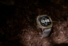 Rugged smartwatch with a round display resting on rocky trail terrain, illuminated by a beam of light.
