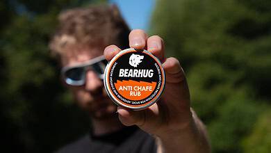 Man holding Bearhug Anti Chafe Rub container towards camera with blurred background.