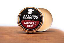 Bearhug Muscle Rub tin on a wooden surface with a blurred background, product label clearly visible.