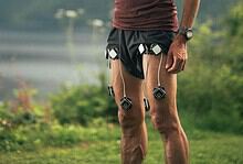 Male runner in outdoor landscape checking his smartphone, with running devices attached to his shorts, mountains in the background.