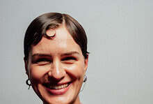 Smiling female runner with short dark hair wearing a black running shirt, showcasing confidence and fitness, against a plain grey background.